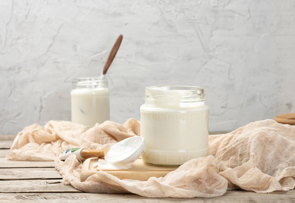 homemade yogurt in a glass transparent jar on a wooden table, a healthy fermented milk product - Photo, Image
