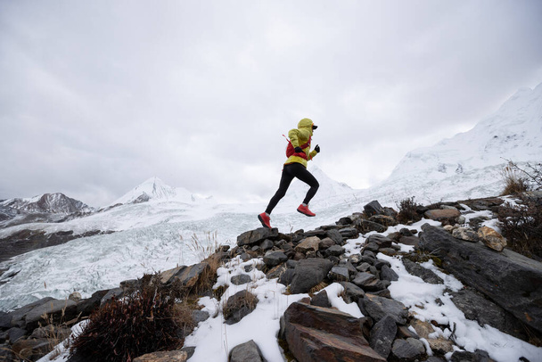 Woman trail runner cross country running up hill to winter snow mountain top - Fotografie, Obrázek