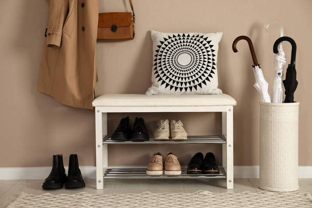 Stylish storage bench with different pairs of shoes near beige wall in hall - Zdjęcie, obraz