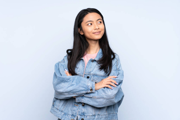 Teenager Chinese woman isolated on blue background looking to the side - Фото, изображение