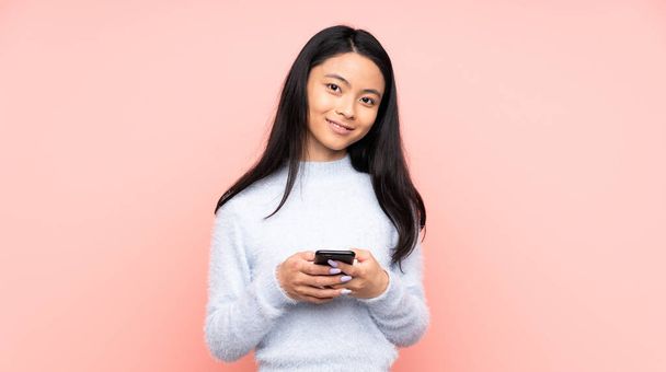 Teenager Chinese woman isolated on pink background sending a message with the mobile - Foto, Bild