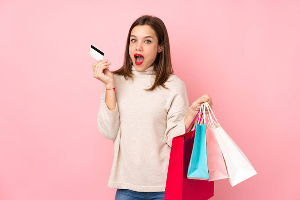 Ragazza adolescente isolato su sfondo rosa tenendo borse della spesa e sorpreso - Foto, immagini