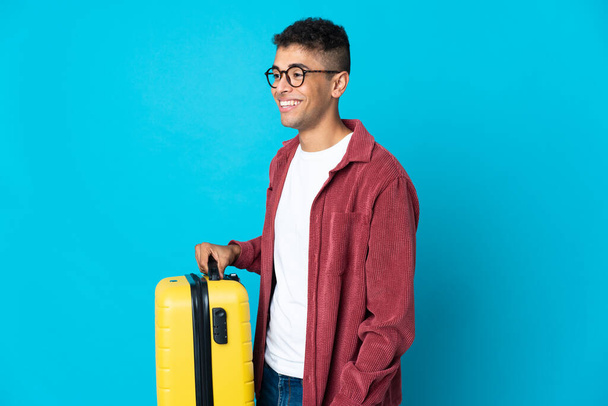 Νεαρός Βραζιλιάνος πάνω από απομονωμένο υπόβαθρο σε διακοπές με ταξιδιωτική βαλίτσα - Φωτογραφία, εικόνα