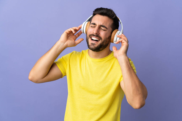 Junger gutaussehender Mann mit Bart isoliert auf lila Hintergrund Musik hören und singen - Foto, Bild
