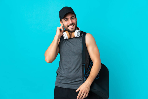 Mladý sportovní muž se sportovní taška izolované na modrém pozadí se směje - Fotografie, Obrázek