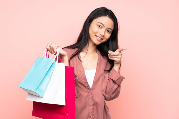Adolescente chino chica aislado en rosa fondo sosteniendo bolsas de compras y con el pulgar hacia arriba - Foto, Imagen