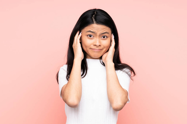 Teenager Chinese woman isolated on pink background frustrated and covering ears - 写真・画像