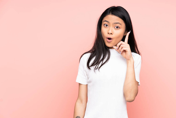 Adolescente chinoise isolée sur fond rose dans l'intention de réaliser la solution tout en levant le doigt - Photo, image
