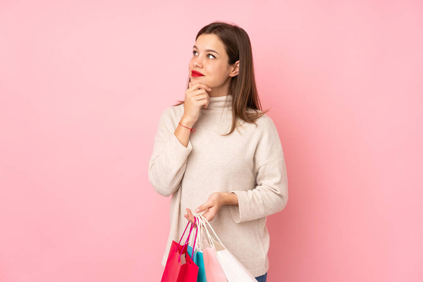 Ragazza adolescente isolato su sfondo rosa tenendo borse della spesa e pensando - Foto, immagini