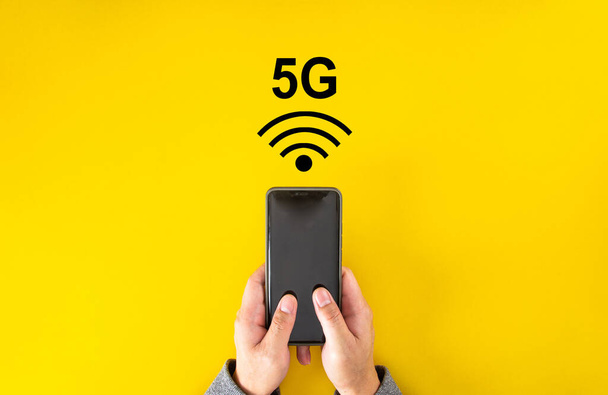 Ανδρικό χέρι κρατώντας smartphone με σήμα 5G σε κίτρινο χρώμα φόντο με αντίγραφο χώρο. - Φωτογραφία, εικόνα