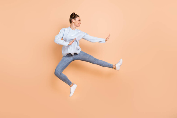 Full size profile photo of optimistic nice brunette lady jump karate wear blue sweater jeans sneakers isolated on beige background - Foto, Imagem