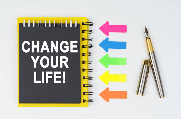 Business and finance concept. On a white background lies a pen, arrows and a notebook with the inscription - CHANGE YOUR LIFE - Foto, Imagen