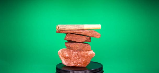 Ένα χέρι έλασης Μαριχουάνα κοινές ισορροπίες πάνω από μια στοίβα από κόκκινη άμμο πέτρα και Himlayan Pink Sea Salt. - Φωτογραφία, εικόνα