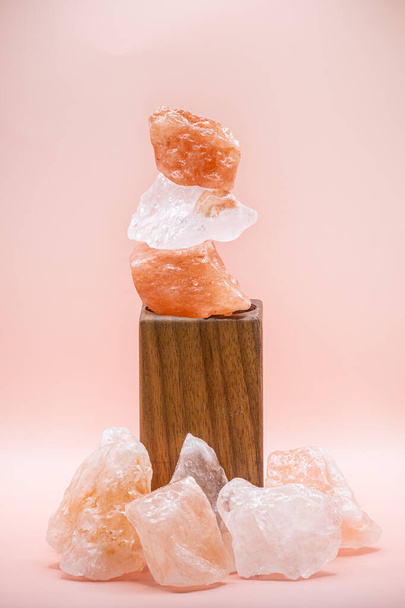 Large chunks of Himalayan sea salt are stacked on top of each other for peace and balance. Supported by a wooden stand and isolated against a soft pink background. - Foto, Imagen