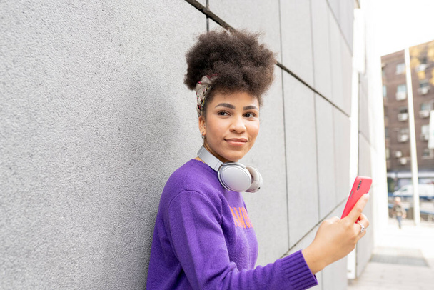 Молода красива жінка, змішана раса на вулиці з навушниками та смартфонами щаслива усміхнена
, - Фото, зображення