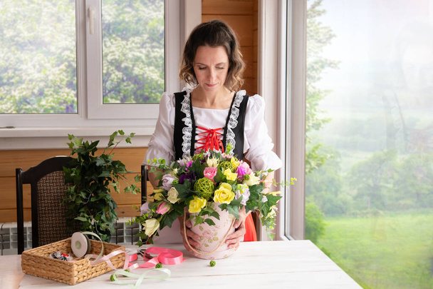 A female florist makes a basket of artificial flowers by the window. - Фото, зображення