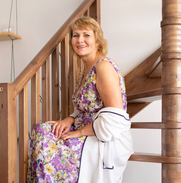 A middle-aged woman is sitting on the stairs in an apartment - Foto, imagen
