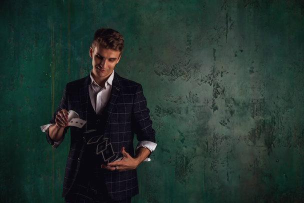 Close-up portrait of young man with gambling cards. Handsome guy shows tricks with card. Clever hands of magician on green texture background. Concept of entertainment and Hobbies. Copy space for site - Фото, зображення