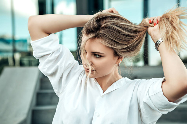 Woman sitting concrete stairs looking away. Lady dressed in white elegant shirt make tails hairdo enjoy new hair smooth hair effect during the quarantine due to coronavirus pandemic. Fashion concept - Photo, Image