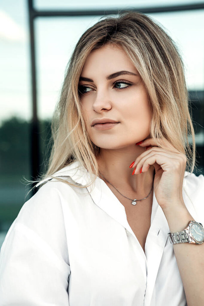 Close up portrait of fashionable pretty woman standing outside look away. Lady dressed in white bright shirt, silver watch on hand. Small business owner near office. Fashion concept. - Foto, imagen