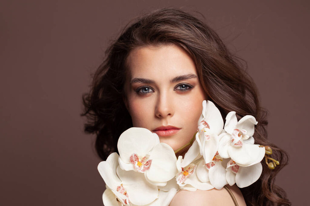 Cara femenina perfecta con piel sana y clara y retrato de flores de orquídea blanca. Tratamiento facial y concepto de cuidado de la piel - Foto, Imagen