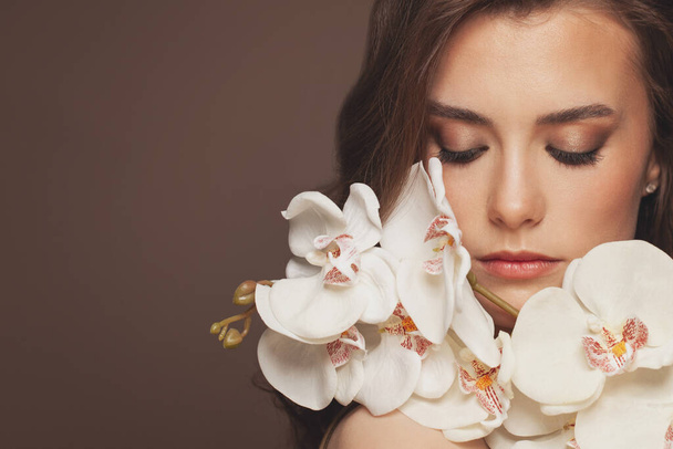 Atrakcyjny model kobiety ze zdrową, czystą skórą i wiosennymi kwiatami storczyków. Koncepcja leczenia twarzy i pielęgnacji skóry - Zdjęcie, obraz