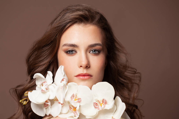Güzel kadın yüzü, sağlıklı kahverengi saçlar, açık ten ve beyaz orkide çiçekleri portresi. - Fotoğraf, Görsel