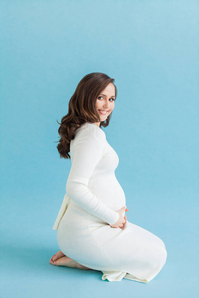 Portret van schattige jonge glimlachende zwangere vrouw op blauwe achtergrond - Foto, afbeelding