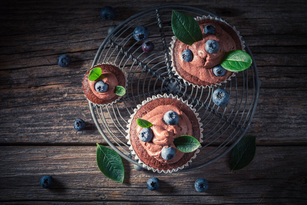 Sweet and chocolate brown cupcake with blueberries and cream. Chocolate cupcake with fruit. Homemade sweets.  - Fotoğraf, Görsel