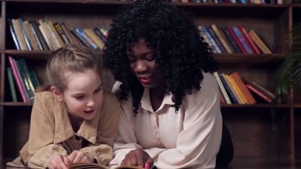 Lady tutor con i capelli ricci insegna scolara lettura libro - Filmati, video