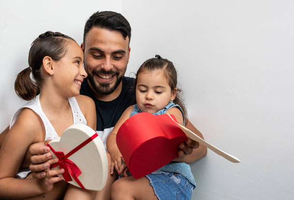 Lachende vader en dochters, openen een geschenk dat ze hebben ontvangen van de meisjes voor Vaderdag - Foto, afbeelding