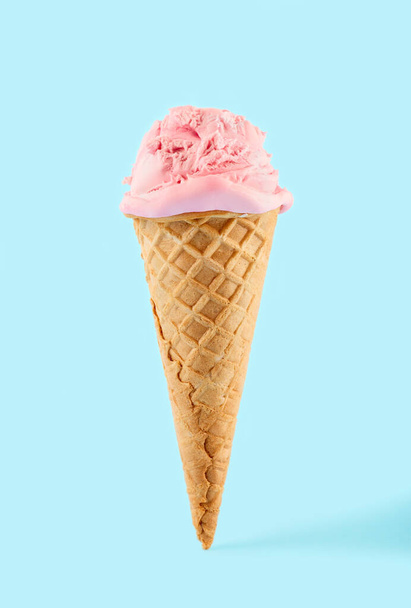 růžová zmrzlina koule v kuželu vafle na modrém pozadí. Ovocná zmrzlina ve vaflovacím kuželu. - Fotografie, Obrázek
