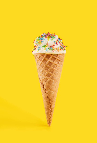 ワッフルコーンの白いアイスクリームボールが黄色の背景にあります。ワッフルコーンのフルーツアイス. - 写真・画像