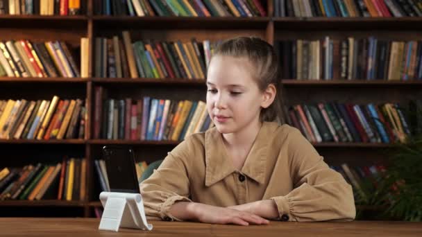 Estudiante junior habla sentado en el escritorio con teléfono inteligente - Metraje, vídeo
