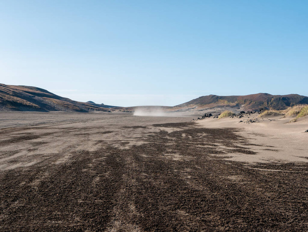 Volcanic rock road to Mutnovsky volcano. Strong wind kicks up swirls of dust on the horizon, making the landscape extraordinary. Kamchatka Peninsula, Russia. - Photo, Image