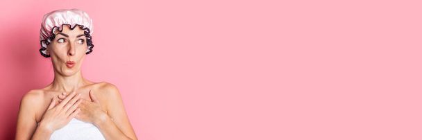 young woman in a pink shower cap looks to the side in surprise on a pink background. Banner - Foto, immagini