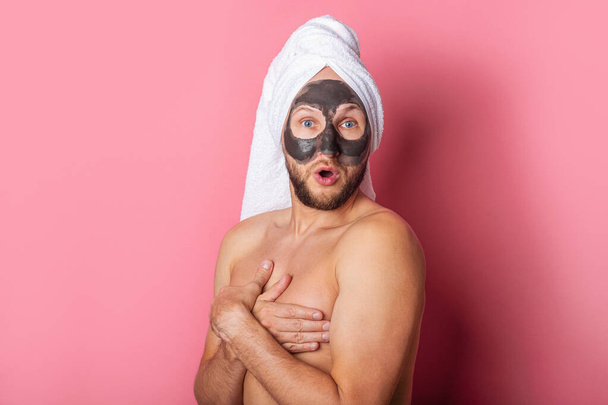 joven sorprendido con una máscara cosmética en la cara, escondiendo su pecho desnudo con las manos sobre un fondo rosa. - Foto, imagen