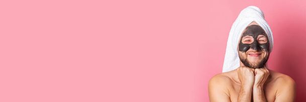 Усмішка молодого чоловіка з косметичною маскою на рожевому фоні. Концепція турботи про шкіру. Банер. - Фото, зображення