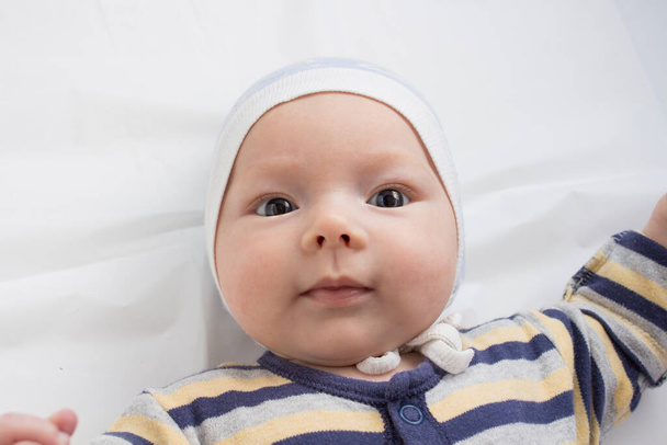 Portrait d'un petit bébé avec une expression drôle visage sur drap blanc. Couché plat, vue du dessus. - Photo, image