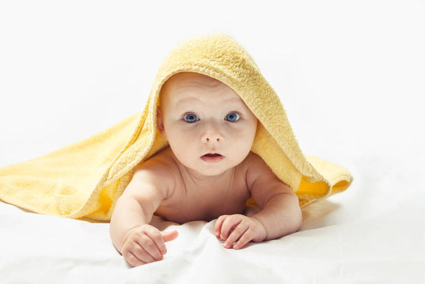 Charming happy child with blue eyes in a yellow towel on a white background. - Photo, Image
