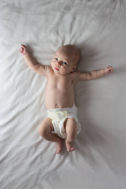 Baby Girl in einer weißen Windel auf einer weißen Decke liegend. Weißer Hintergrund. Flache Lage, Draufsicht. - Foto, Bild