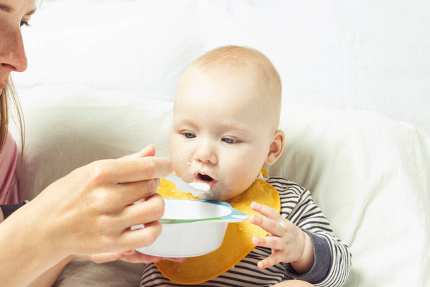 Genç bir anne küçük bir çocuğu kaşıkla besler. Bebeği katı gıdayla beslemeye başlama kavramı. - Fotoğraf, Görsel