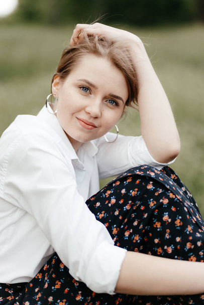 A young stylish girl sits smiles, hugging her head against a background of grass and looking at the camera. Close-up photo. High quality photo - Valokuva, kuva