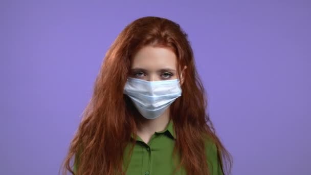 Woman with protective facial mask showing yes sign, nods her head approvingly and then negatively. Young girl, body language concept. Violet studio background. - Video