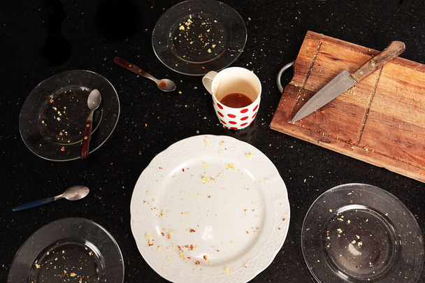 Top view of plates, wooden board and dirty cup with leftover cake, on a black table. Crumbs scattered everywhere and scattered utensils. Appearance that the meal was just finished and there is nothing left. - Zdjęcie, obraz