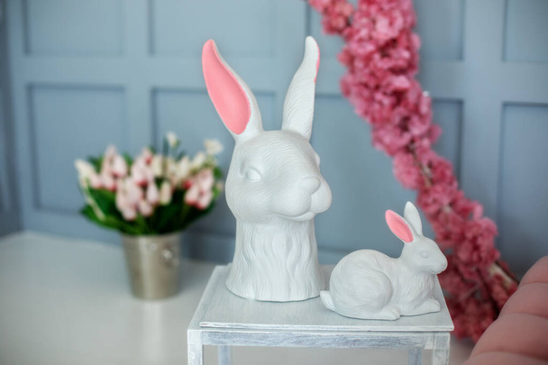 Deux lapins de Pâques statuette en céramique se tiennent sur une table en bois blanc. Maison intérieure de Pâques. Concept de chasse de Pâques. Figurines de lapins blancs et fleurs printanières. Lapin en porcelaine. Concept de décoration de Pâques - Photo, image
