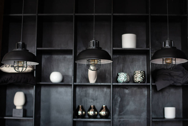 Metal chandeliers in retro style on background wooden shelves with decor. Dark room with Three modern lamps over table. Three modern black ceiling lamps hang in room, close-up. Loft room interior.  - Photo, Image