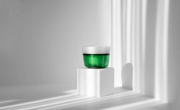 Product concept for beauty and body care on white 3d podium. Green cream jar on foam square. Shadows on the wall from the harsh sunlight in the form of stripes. Mock up for your ad. - Foto, afbeelding