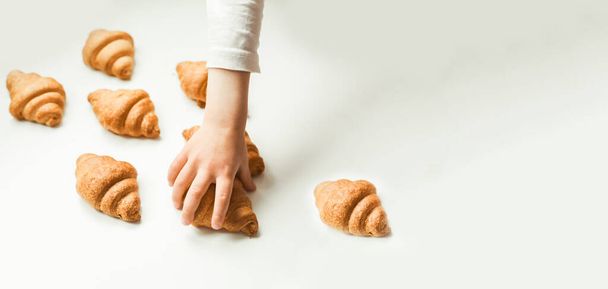 Fresh croissants on the white background. Little girls hand reaching out homemade pastry - Photo, Image