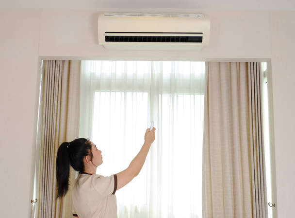 Joven camarera de Asia aire acondicionado al aire libre por control remoto en la habitación del hotel  - Foto, imagen